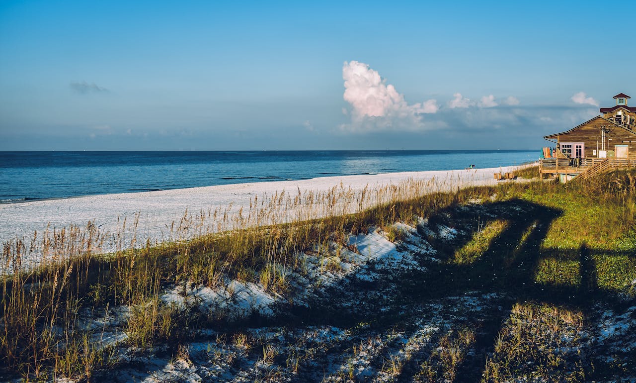 Scenic beach view with a house, blue skies, and ocean waves on a sunny day.